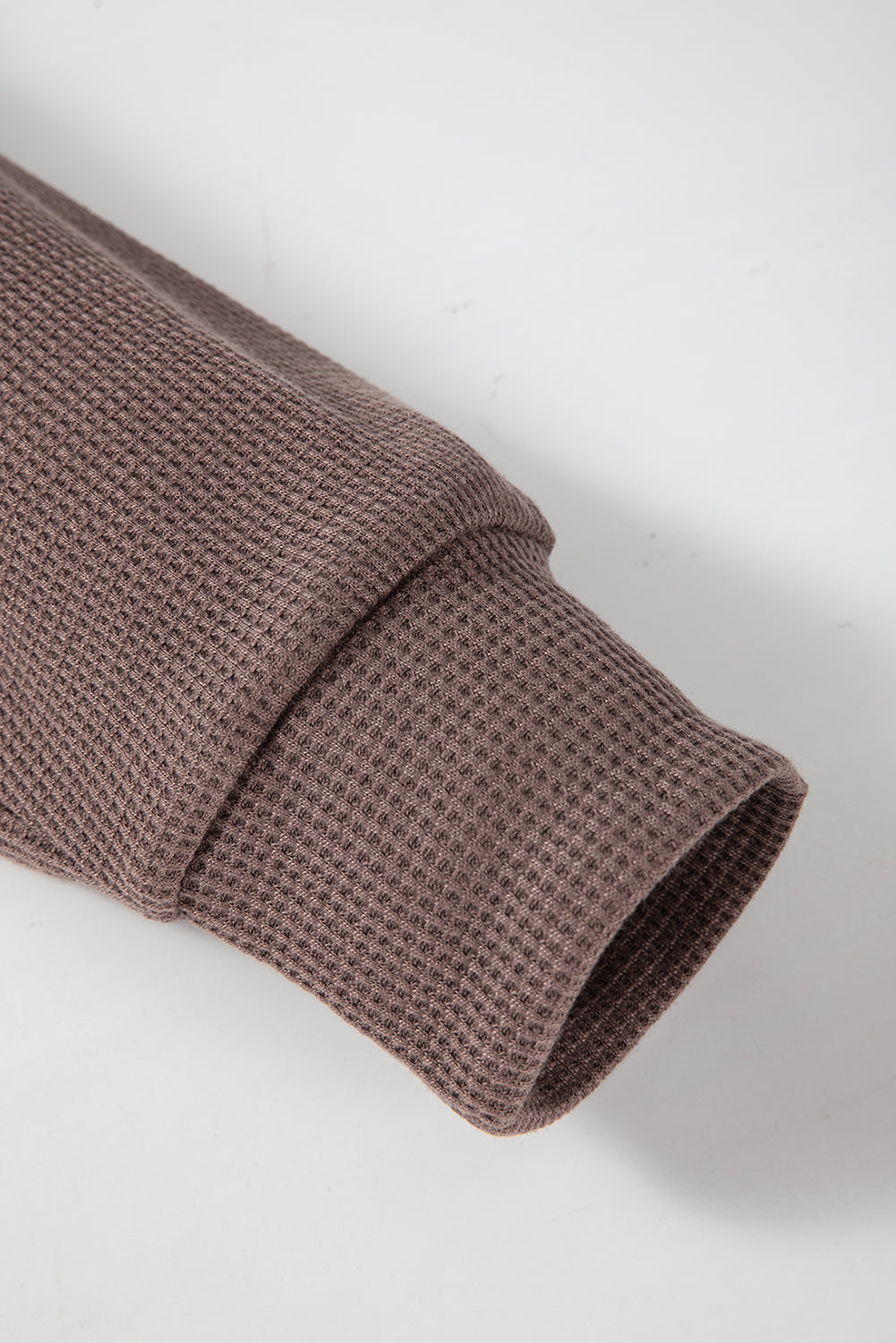 A woman with long hair is standing in profile, wearing a Coffee Waffle Knit Fleece Lined High Low Oversized Hoodie and black shorts. The background is a plain light gray.