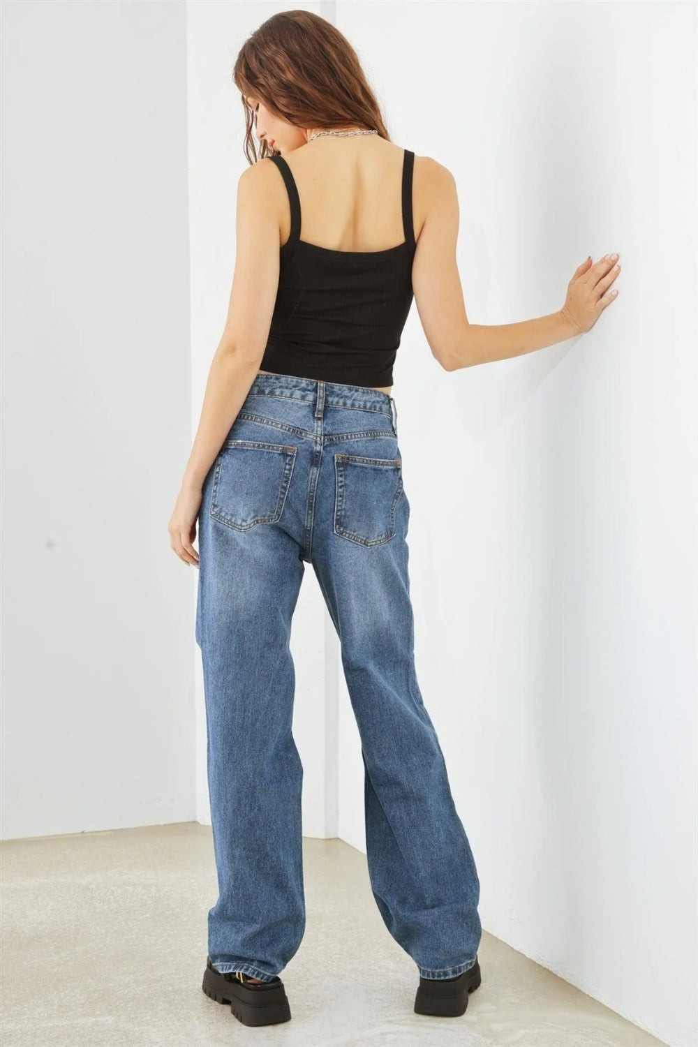 Person wearing HAMMER COLLECTION Distressed High Waist Jeans with ripped knees and black platform sandals, standing in a minimalist setting. The flattering fit and edgy distressed details add to the overall chic look.