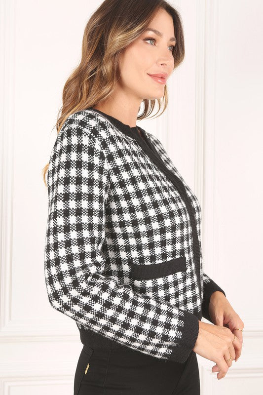 A woman dressed in the Black Check Knitted Jacket, featuring snap buttons and functional pockets, complemented by black pants, stands against a white background.