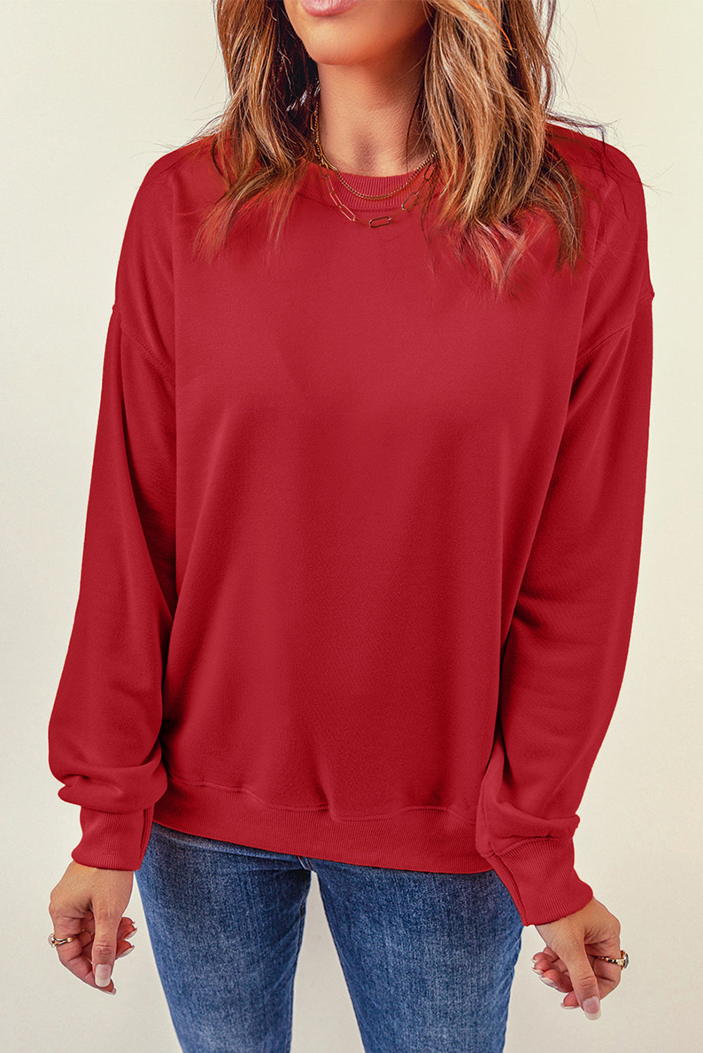 A person wearing a long-sleeved red shirt and blue jeans stands with their back to the camera, one hand resting on their hip, as if showcasing a cozy Fiery Red Plain Crew Neck Pullover Sweatshirt for winter.