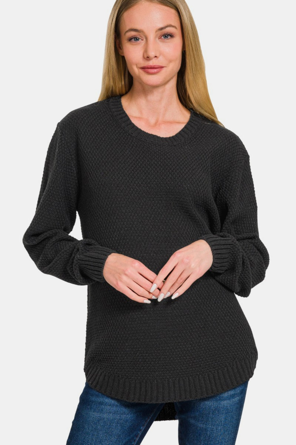 A woman with long hair is wearing the Zenana Full Size Round Neck Long Sleeve Curved Hem Sweater paired with jeans, standing against a plain background.