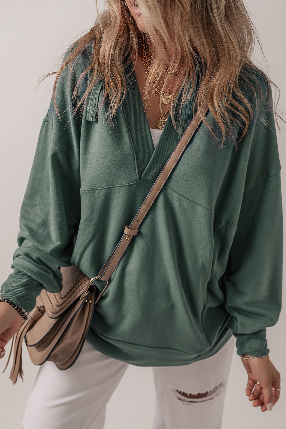 A person with long, wavy hair wearing a Sea Green Casual V Neck Drawstring Hoodie and white pants, carrying a brown crossbody bag. The person's back is facing the camera.