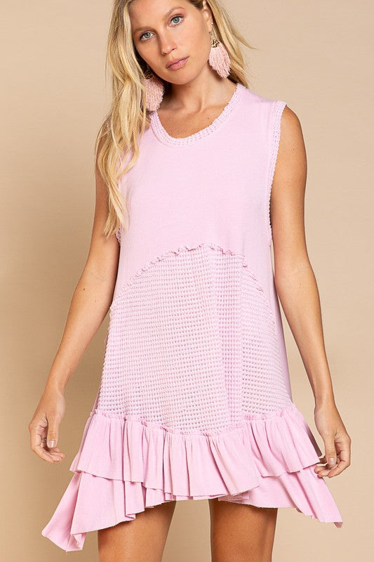 A woman in a Sleeveless Ruffle Hem Dress featuring textured patterns poses against a beige background. Her long blonde hair flows down, and she wears large pink earrings, emphasizing the baby doll fit that perfectly complements her style.