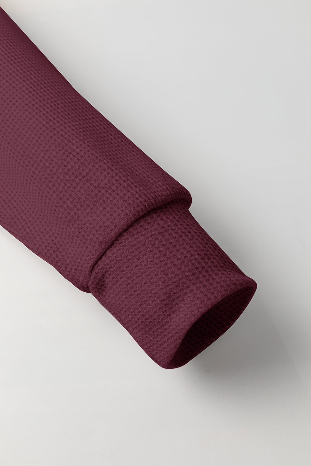 A woman in a Red Dahlia Waffle Knit Fleece Lined High Low Oversized Hoodie and black shorts is seen from behind, standing against a plain gray background.