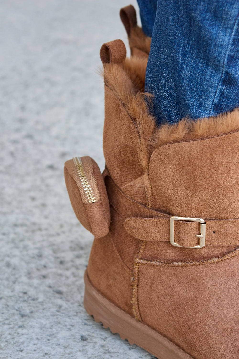 Person wearing ripped blue jeans and Forever Link Plush Thermal Flat Boots, tan in color, fur-lined with side buckles, standing on a concrete surface. These stylish boots promise cozy insulation for the feet.