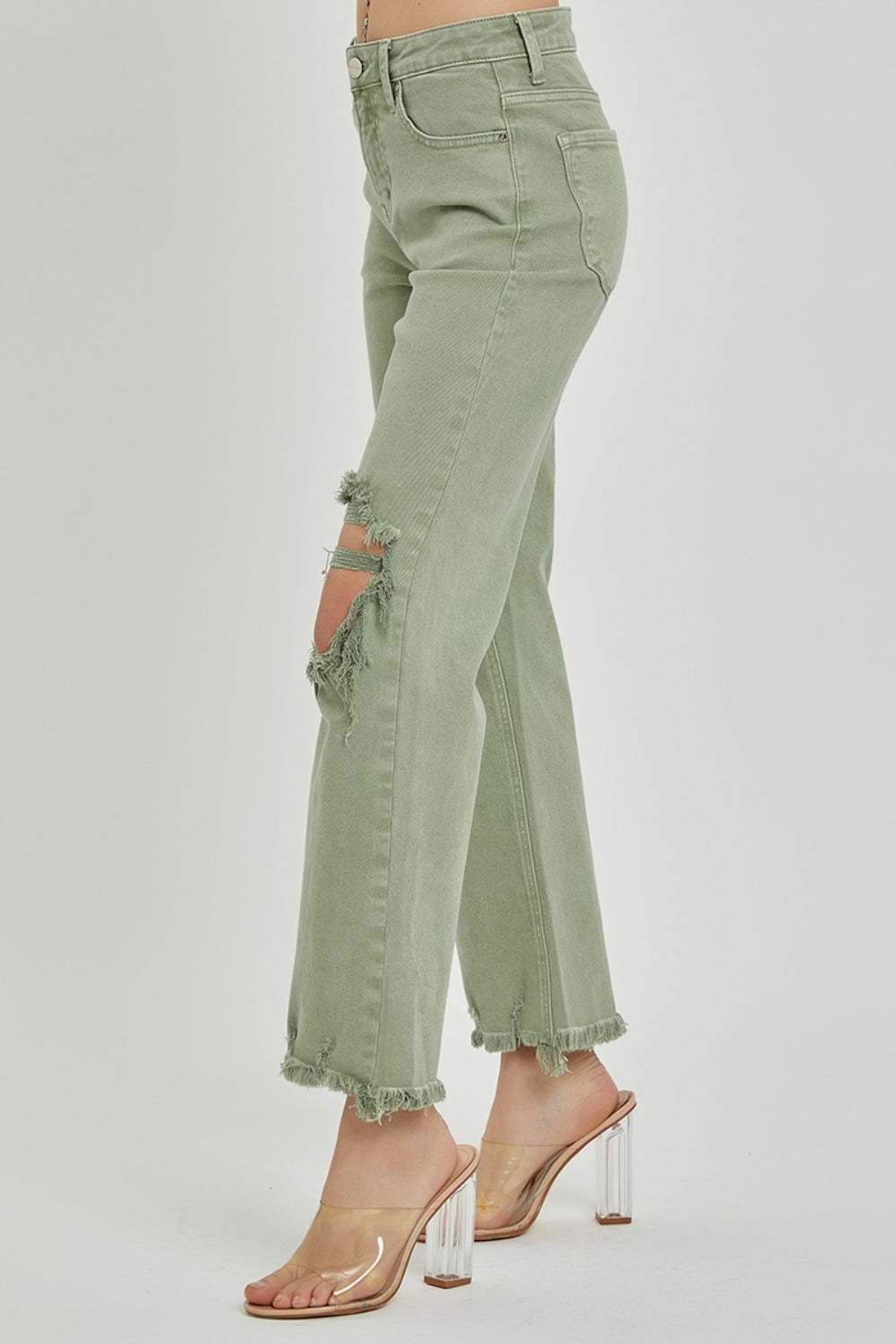 A person wearing RISEN light green distressed ankle bootcut jeans with frayed hems and a beige long-sleeved top, shown from midsection to feet.