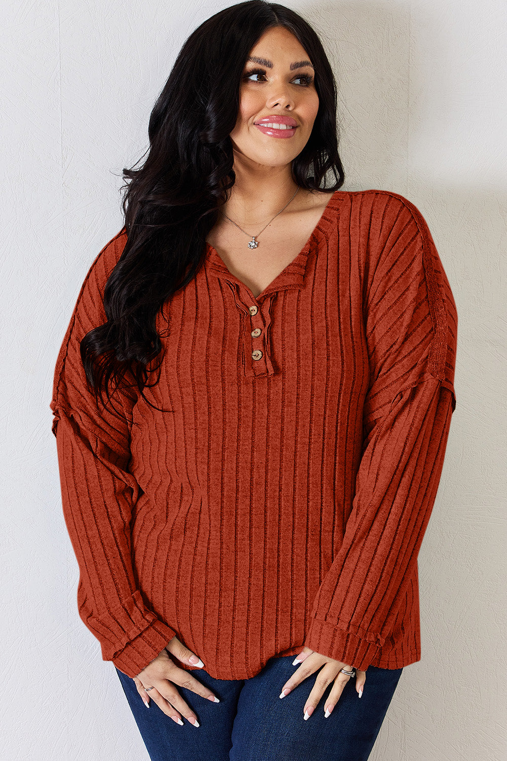 A woman with long, wavy blonde hair wears a slightly stretchy, textured Basic Bae Full Size Ribbed Half Button Long Sleeve T-Shirt in pink, standing against a neutral backdrop.