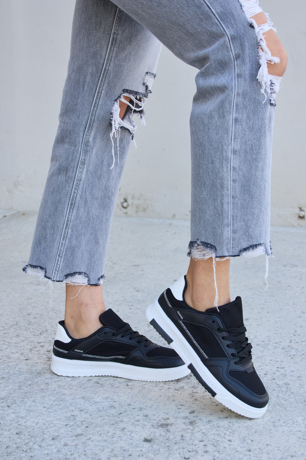 Forever Link Lace-Up Round Toe Flat Sneakers with white soles, styled with ripped gray jeans on a concrete surface.