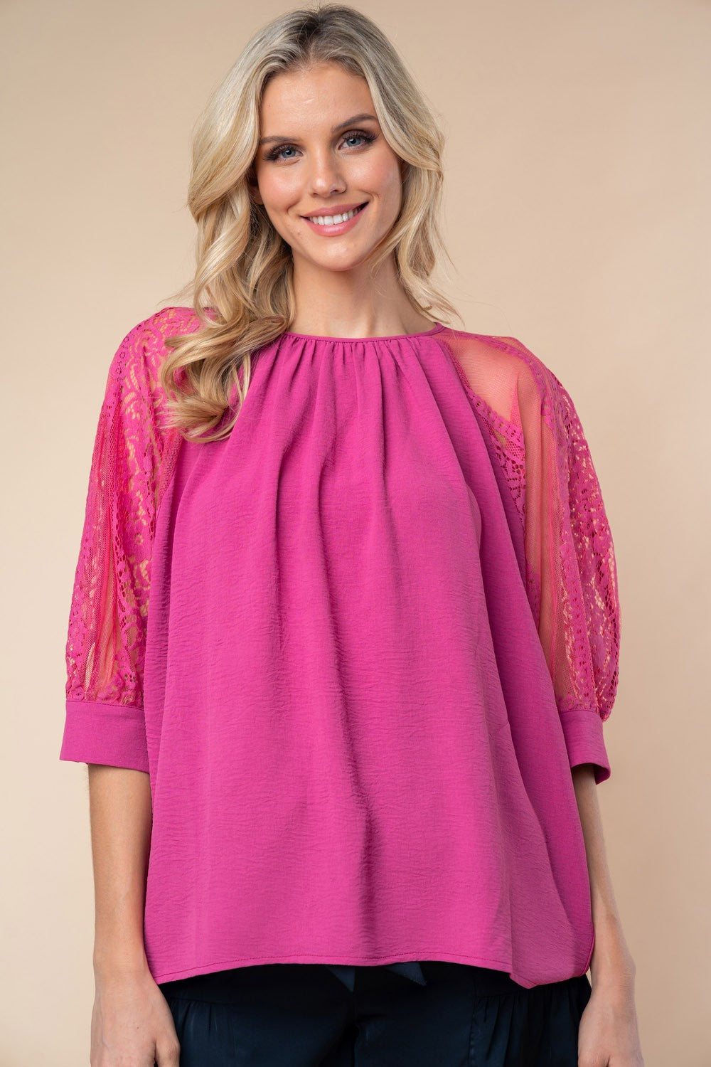 A person stands against a neutral background, wearing the White Birch round neck blouse with vibrant pink lace half sleeves.