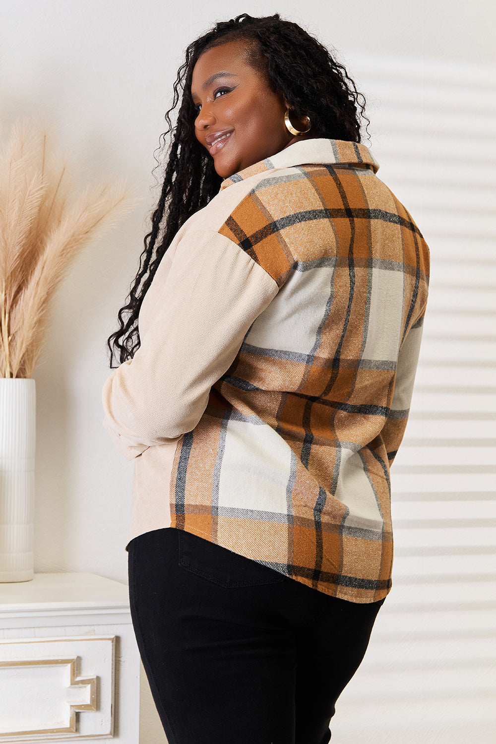 A person wearing the Perfee Plaid Print Dropped Shoulder Shirt and dark pants stands near a white table with a vase of pampas grass, facing slightly away from the camera and smiling, capturing the relaxed vibe of a casual occasion.