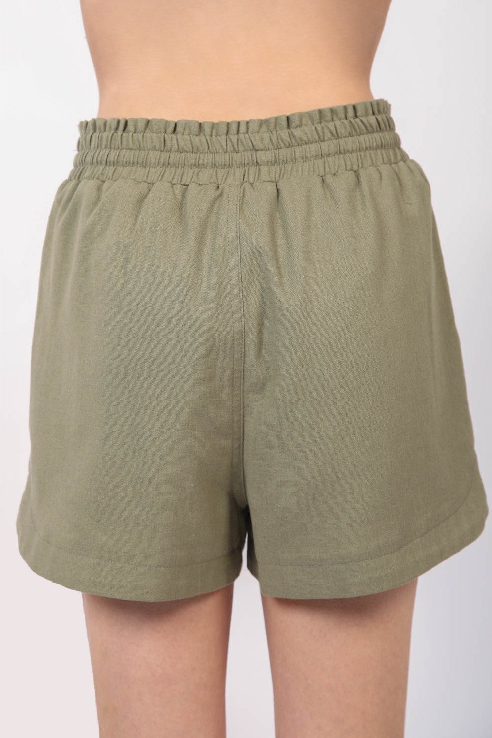 Close-up of a person wearing VERY J Drawstring Elastic Waist Linen Shorts in olive green, featuring two front pockets.