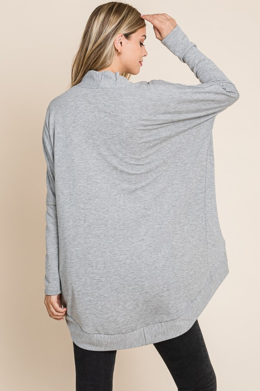 A woman wearing a white shirt, black jeans, and a versatile layering piece—the BOMBOM Open Front Long Sleeve Cocoon Cardigan in grey—stands against a plain beige background.