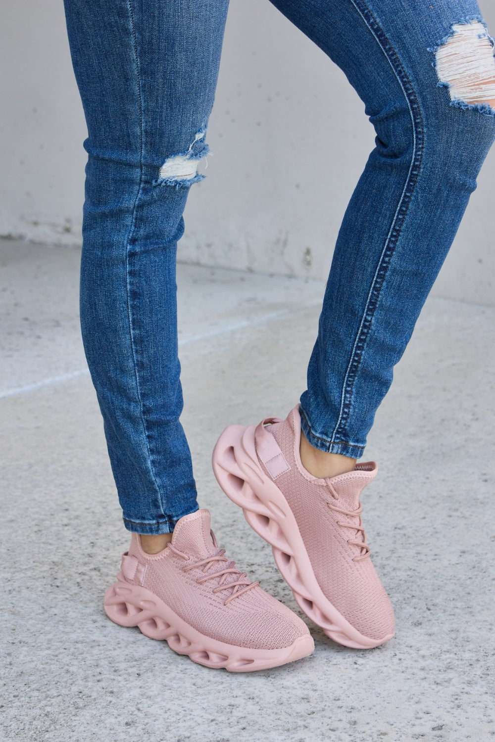 Person wearing blue ripped jeans and Forever Link Mesh Breathable Platform Athletic Shoes in light pink, standing on a concrete surface.