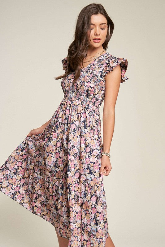 A person in a Vintage Garden Floral Flutter Smocking Midi Dress is standing, holding one side of the dress, and looking down.