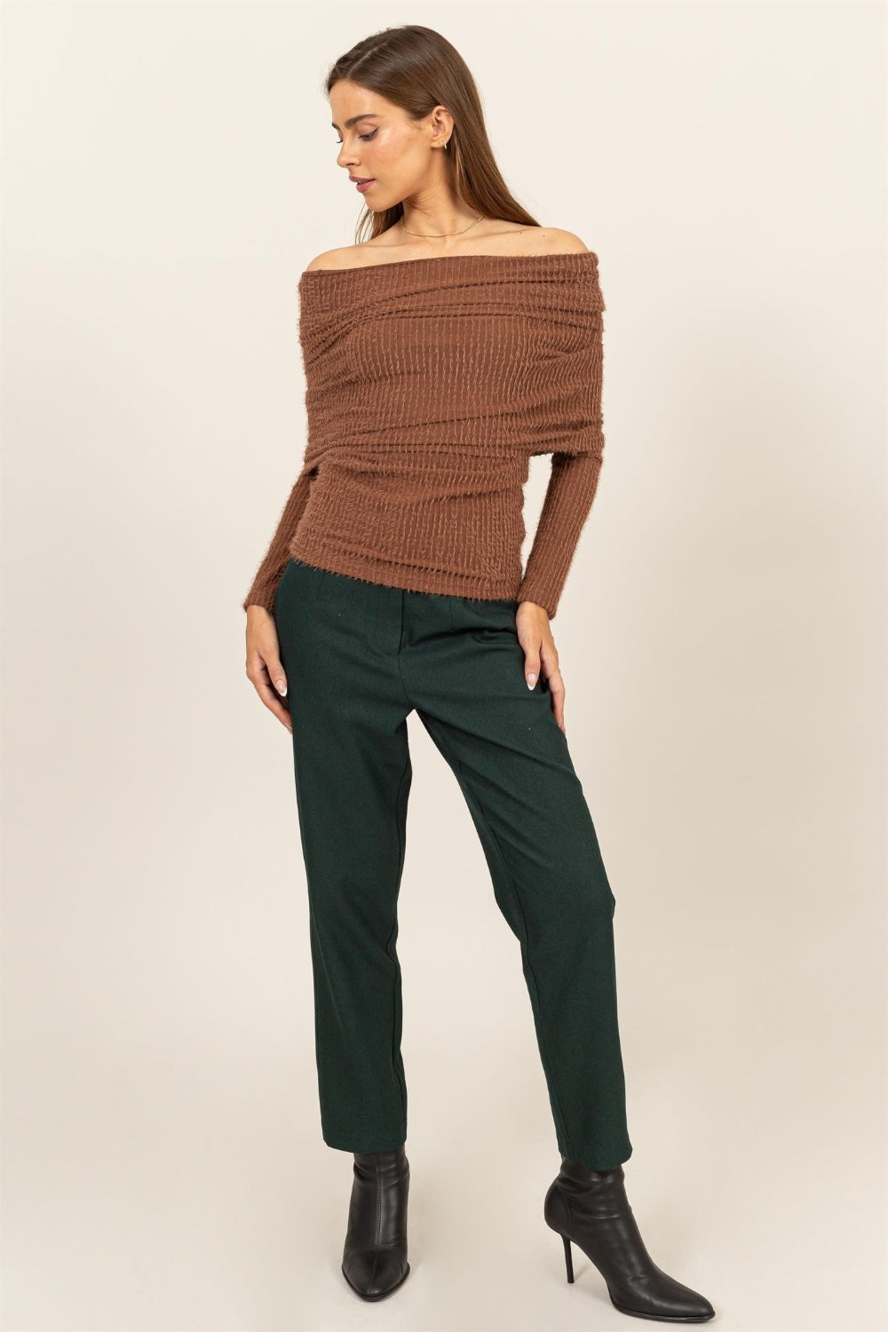 A woman in a HYFVE Fuzzy Off Shoulder Textured Knit Top and dark green pants, facing slightly sideways.