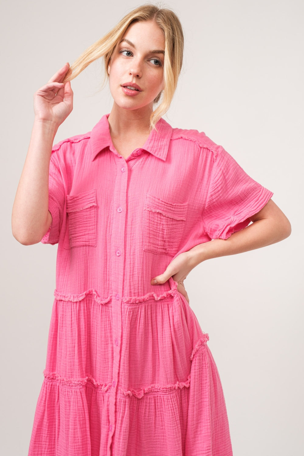 A person wearing the And The Why Full Size Raw Edge Washed Tiered Shirt Dress and light brown heels stands with hands on hips against a neutral background.