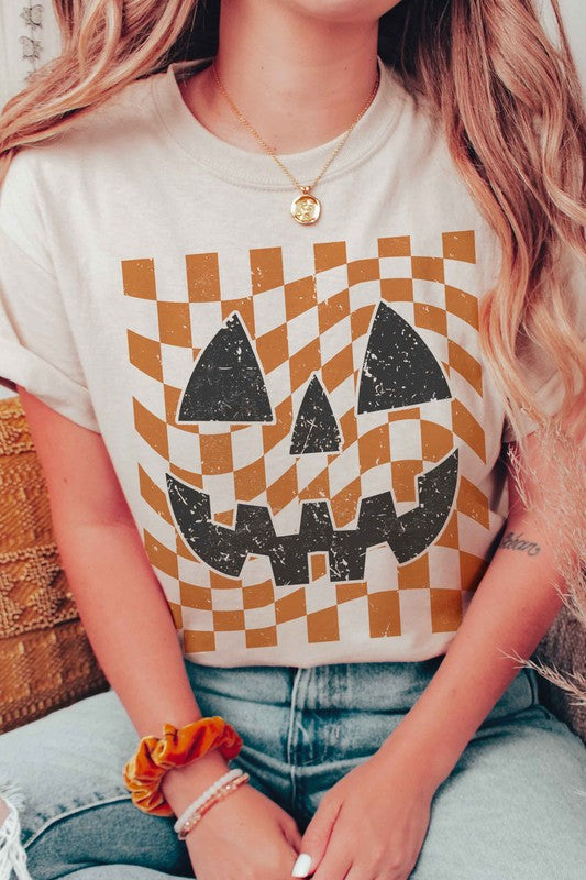 Person wearing a CHECKER PUMPKIN FACE Graphic Tee, made from 100% cotton, paired with high-waisted blue jeans.