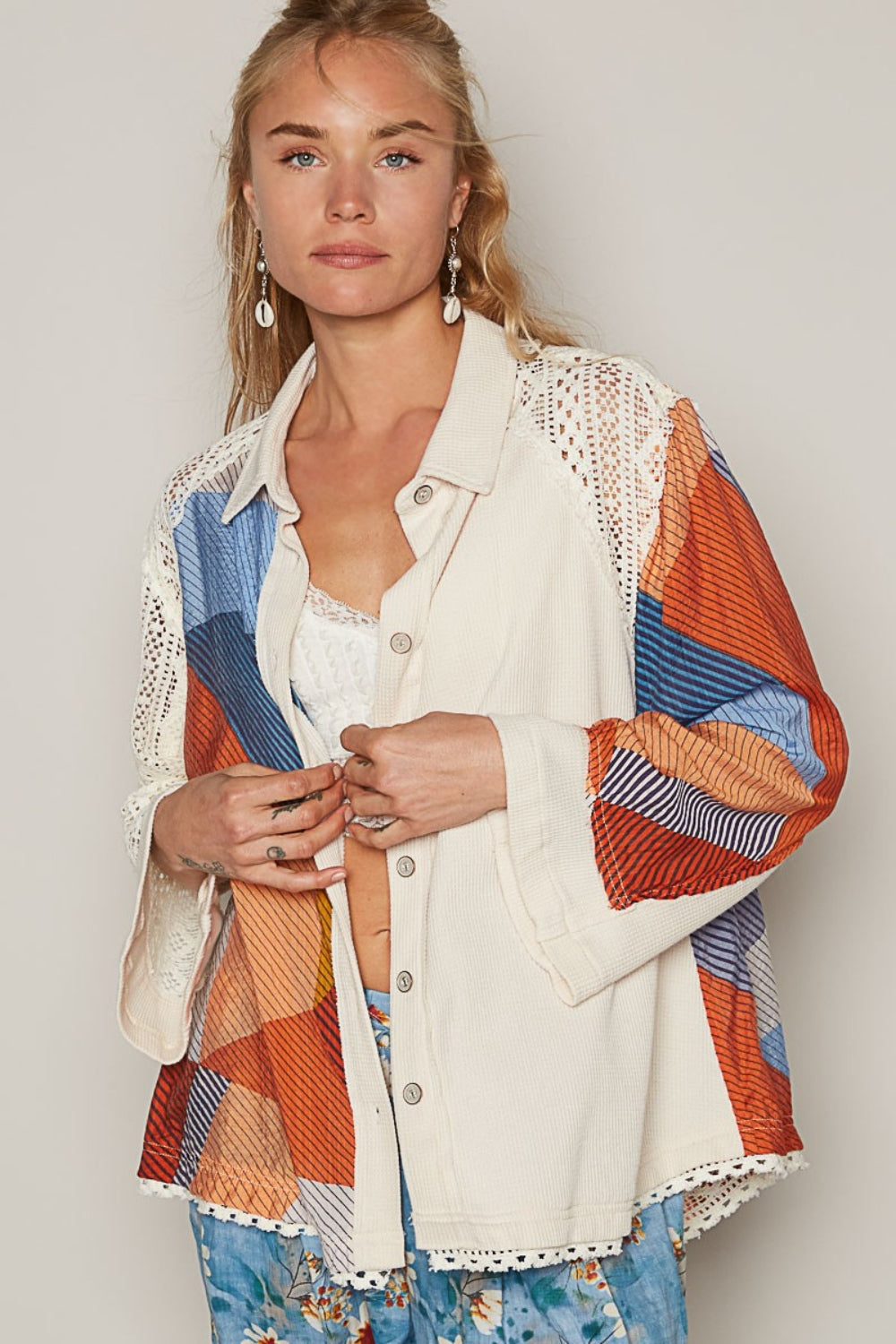 A person stands outdoors in a POL Color Block Crochet Long Sleeve Shirt, exuding a relaxed expression. The coastal background features palm trees and distant buildings.