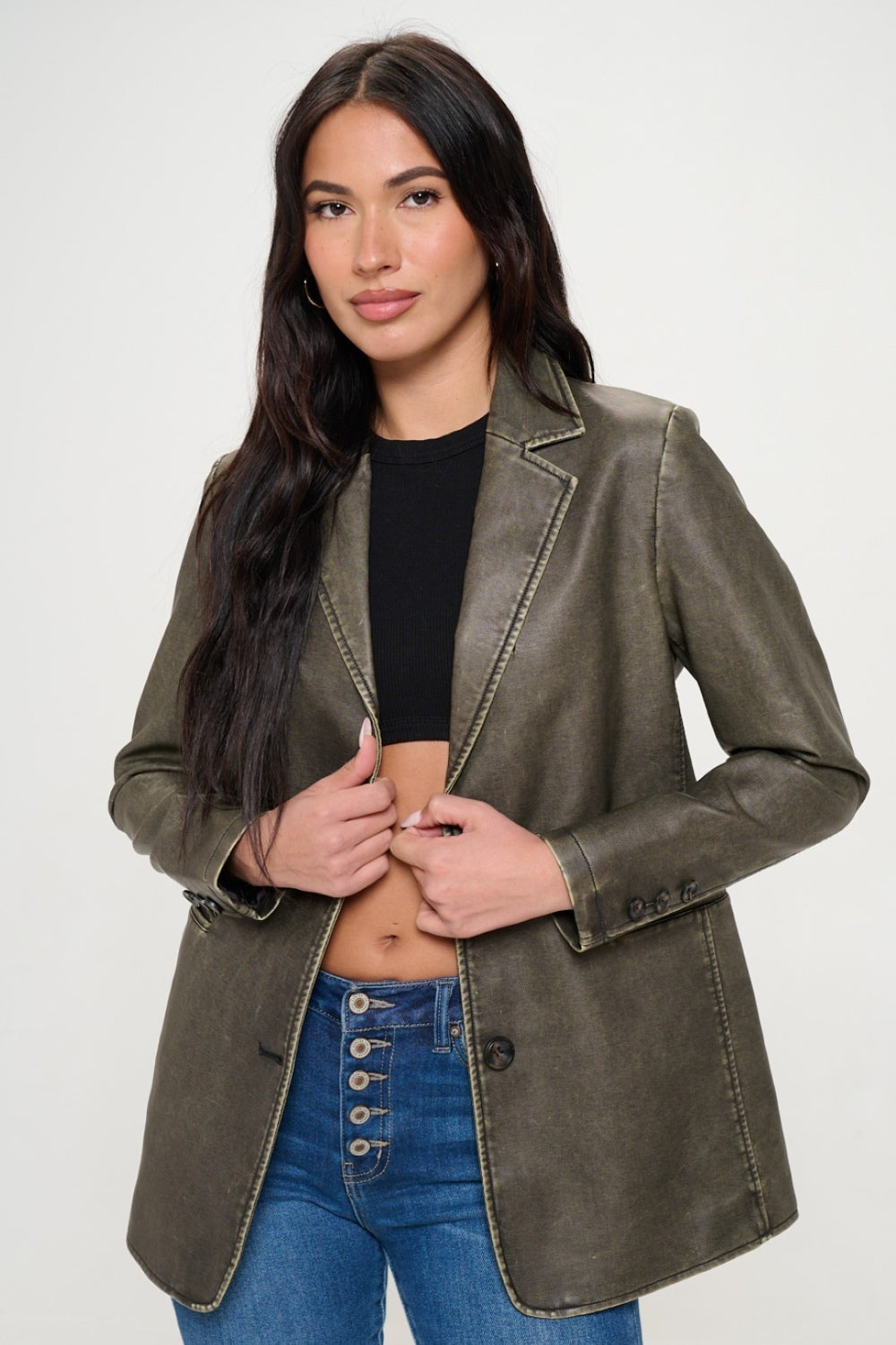 A person with long dark hair wears the Coalition LA Single-Breasted Vegan Leather Blazer in olive green over a black crop top and blue jeans against a neutral background, showcasing a stylish and ethical fashion choice.