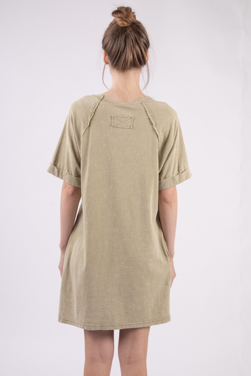 A woman in a VERY J Washed Round Neck Mini Tee Dress poses gracefully against a plain background. Her casual ensemble features an oversized beige tee dress complete with a pocket, radiating effortless style and comfort.