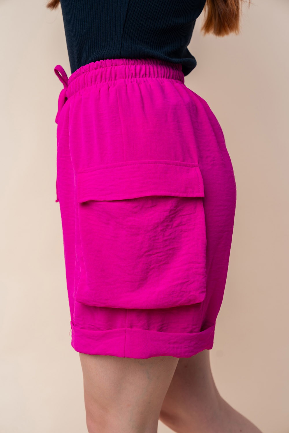 A person is wearing the White Birch High Waisted Drawstring Knit Cargo Shorts in bright pink, featuring side pockets and a drawstring waistband.