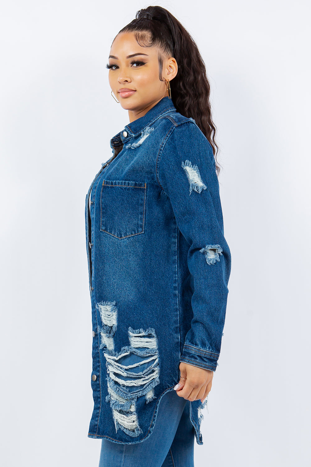 A woman is wearing an American Bazi Distressed Button Up Long Sleeve Denim Jacket over a white top and distressed jeans, posing against a plain background. The denim jacket adds an edgy touch to her chic ensemble.