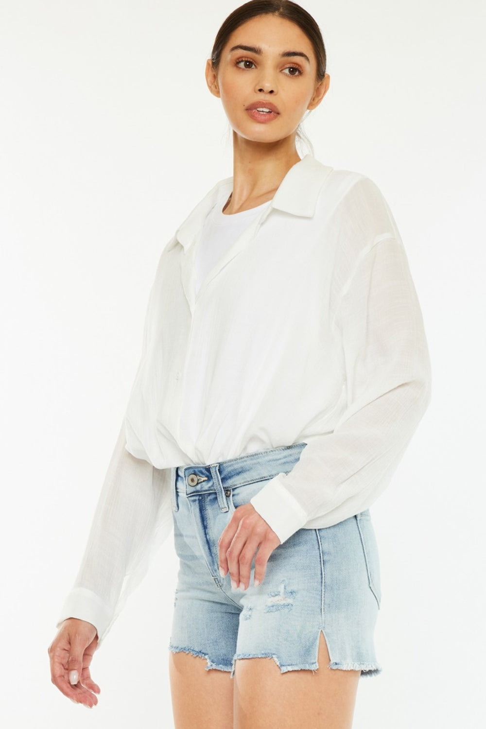 A person wearing a white shirt and the chic Kancan High Rise Side Slit Denim Shorts stands against a plain background, showcasing a perfect addition to any summer wardrobe.