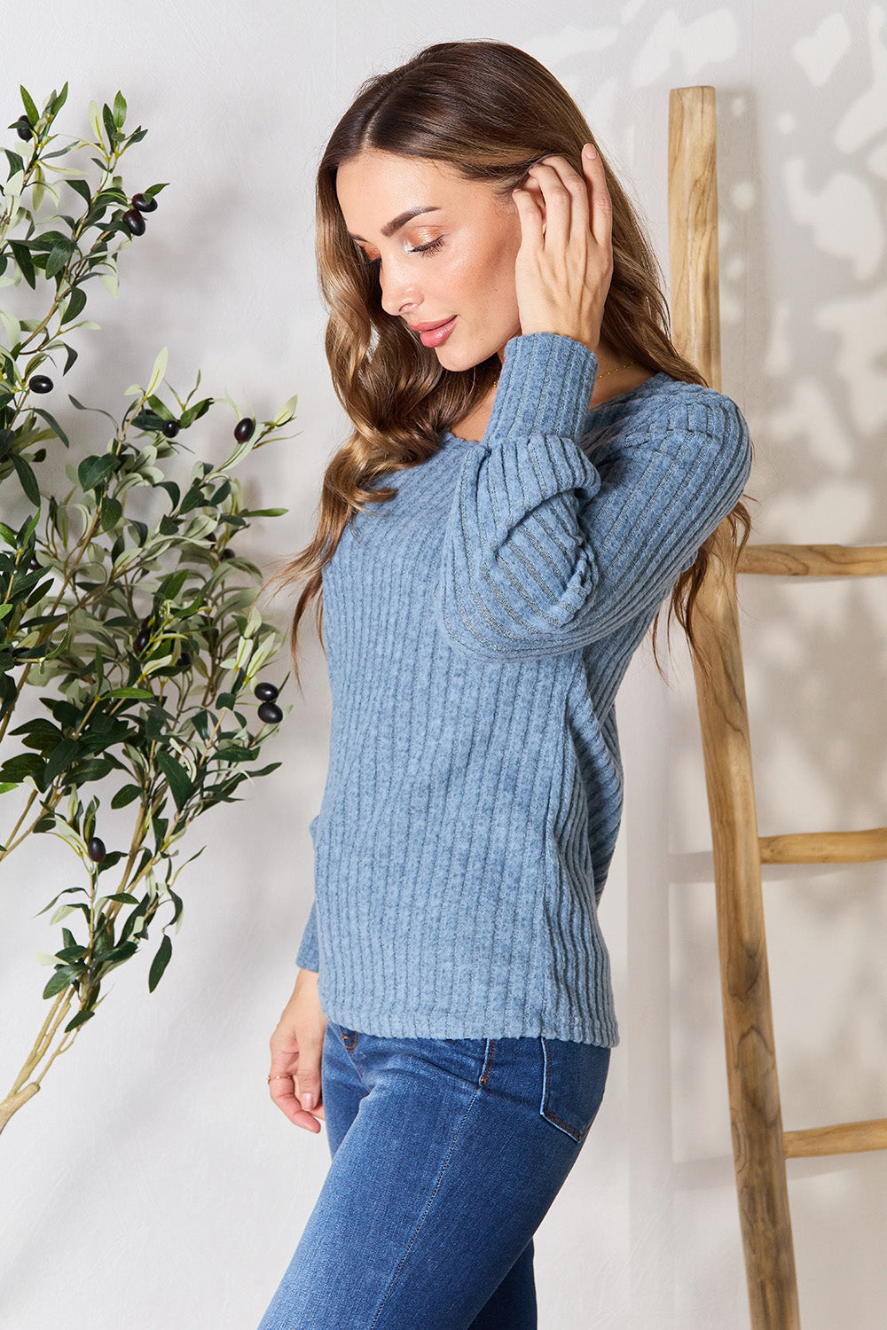 A person in a stylish maroon Ribbed Round Neck Lantern Sleeve Blouse and jeans stands by a wooden ladder, with olive branches in the background.