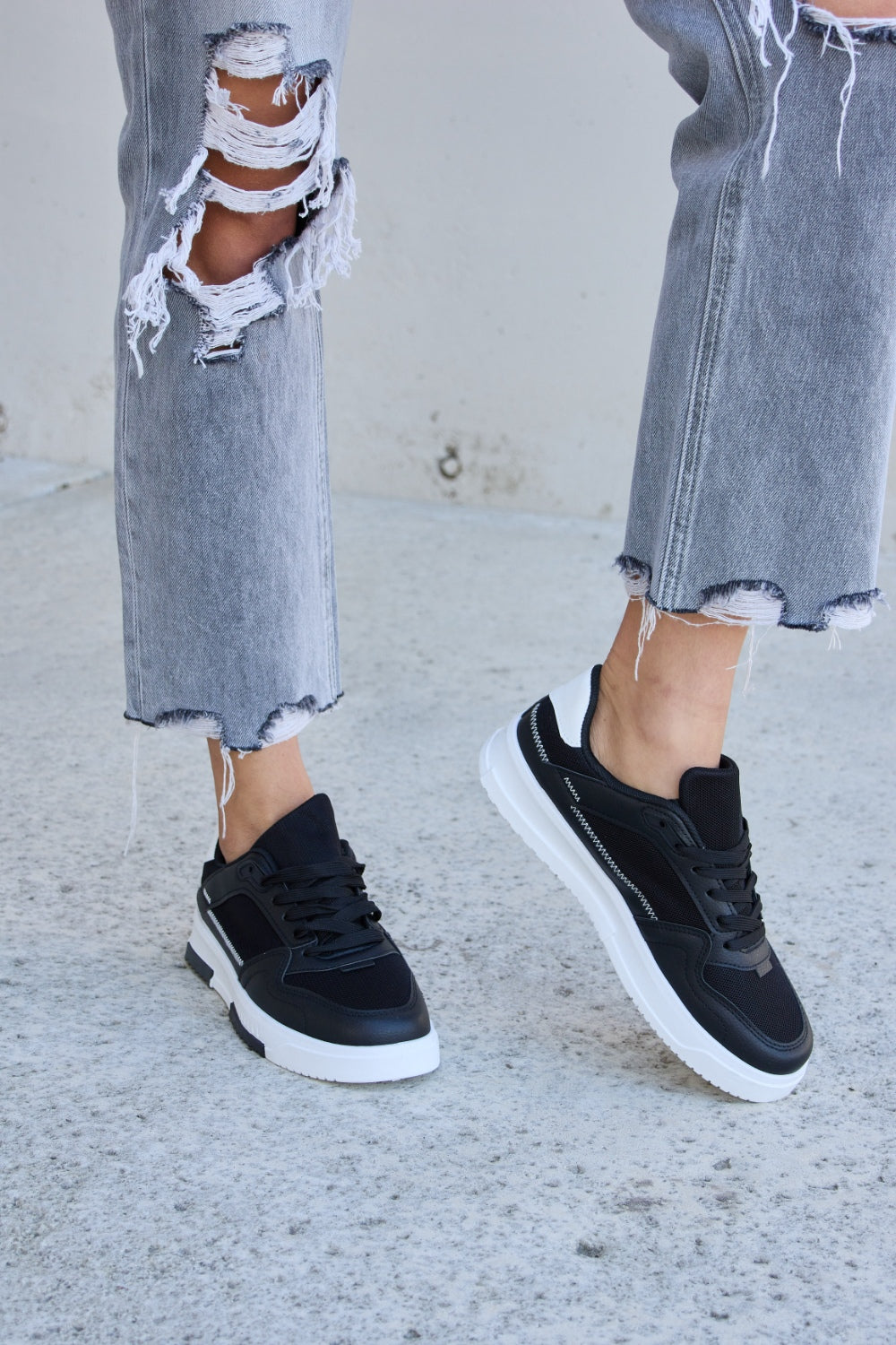 Forever Link Lace-Up Round Toe Flat Sneakers with white soles, styled with ripped gray jeans on a concrete surface.