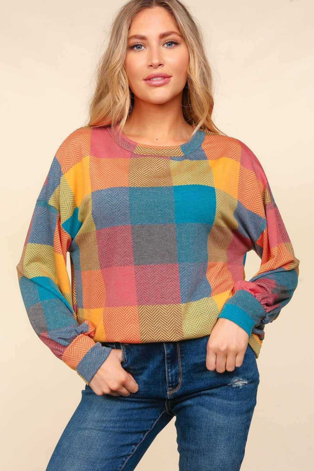 A woman wearing a stylish Haptics Round Neck Color Block Plaid Top and blue jeans poses against a beige background.