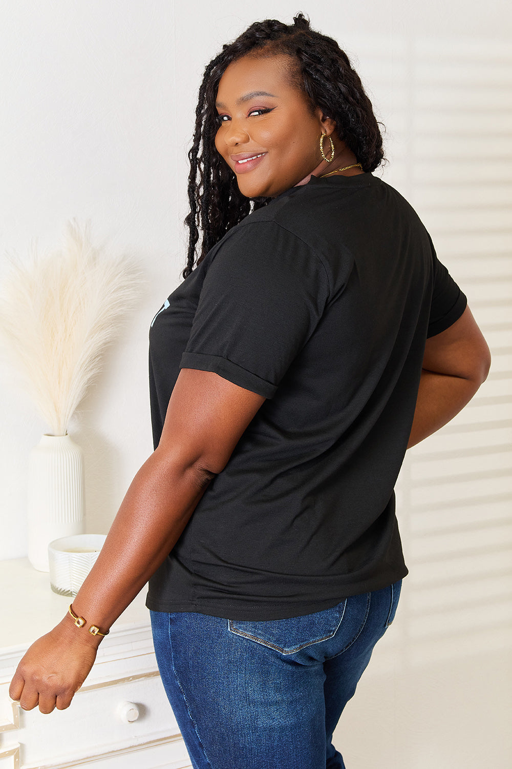 A woman with long braided hair, wearing the Simply Love Slogan Graphic Cuffed Sleeve T-Shirt that says "Established Expensive & Difficult When I Was Born," stands with one hand in her pocket. The trendy cuffed sleeves of her shirt add an extra touch of style.