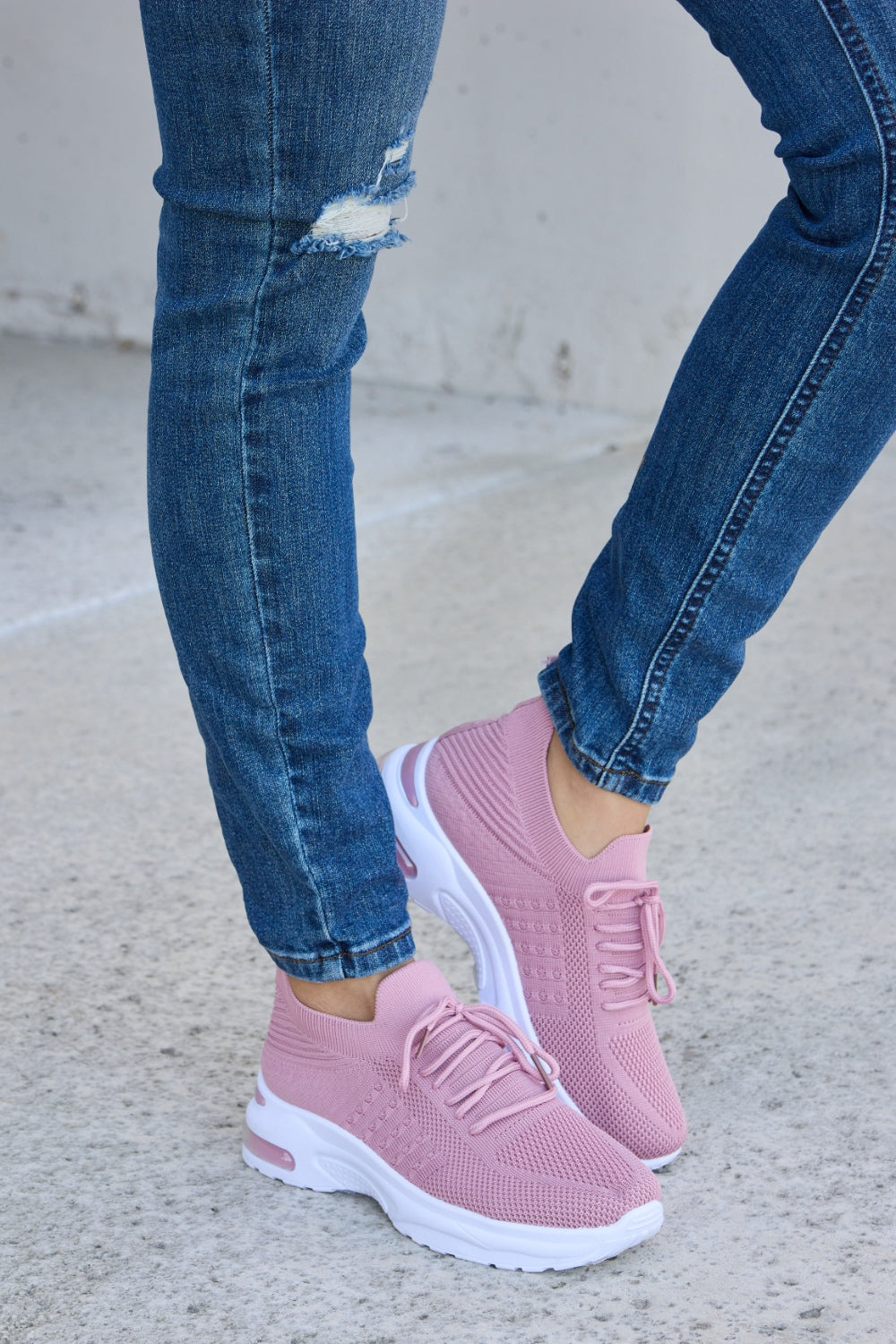 A person is wearing ripped blue jeans and Forever Link breathable mesh lace-up round toe athletic shoes, standing on a concrete surface.