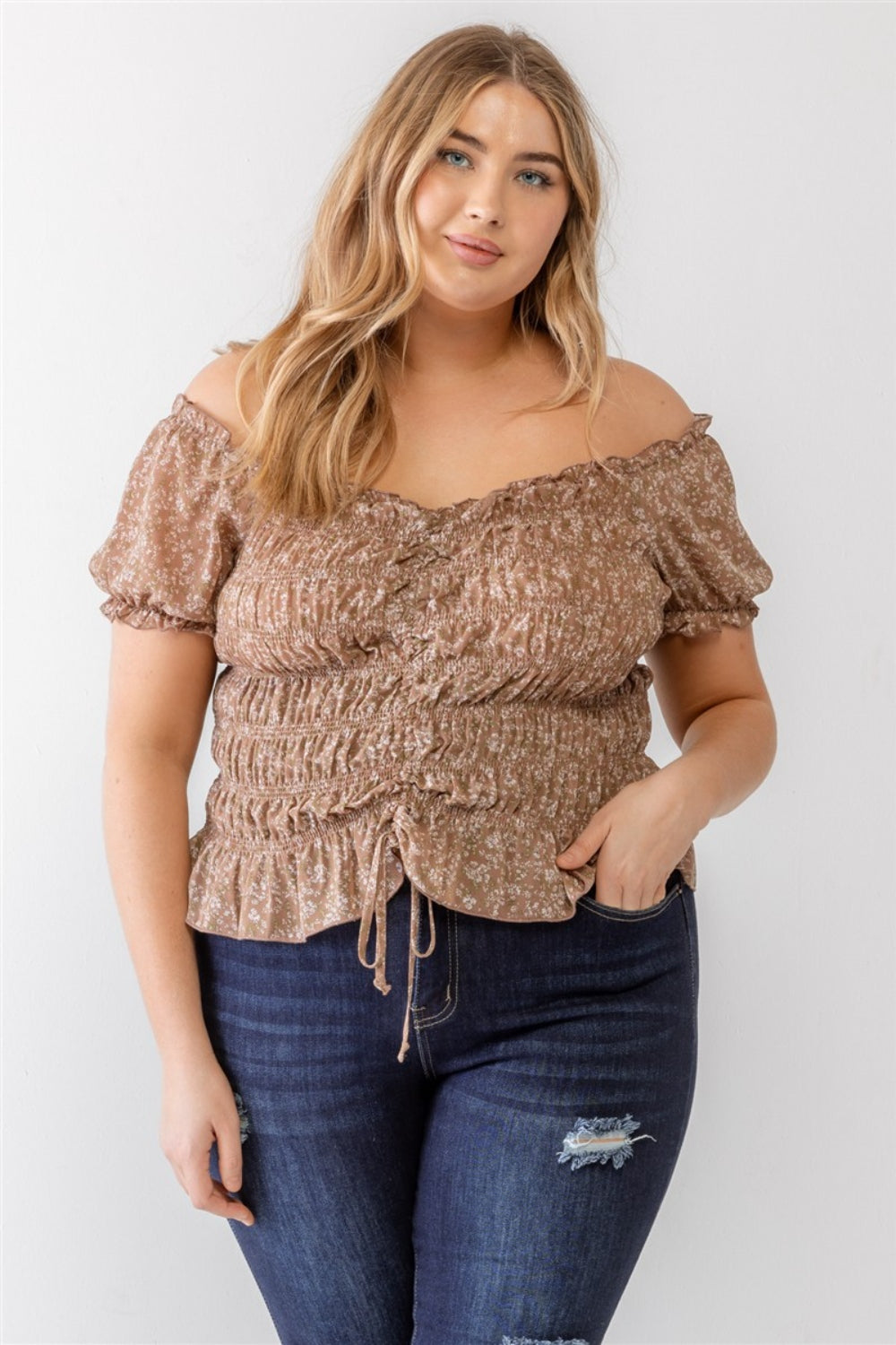 Wearing the Zenobia Plus Size Frill Ruched Off-Shoulder Short Sleeve Blouse and ripped jeans, a person with long hair poses against a plain white background.