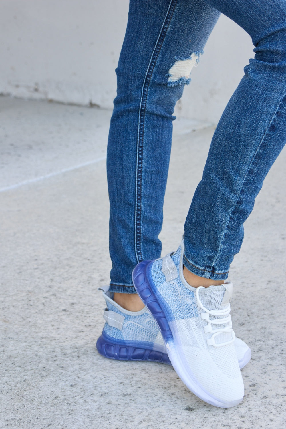 A person wearing distressed blue jeans and a pair of Forever Link Gradient Lace-Up Mesh Breathable Athletic Shoes, standing on a concrete surface.