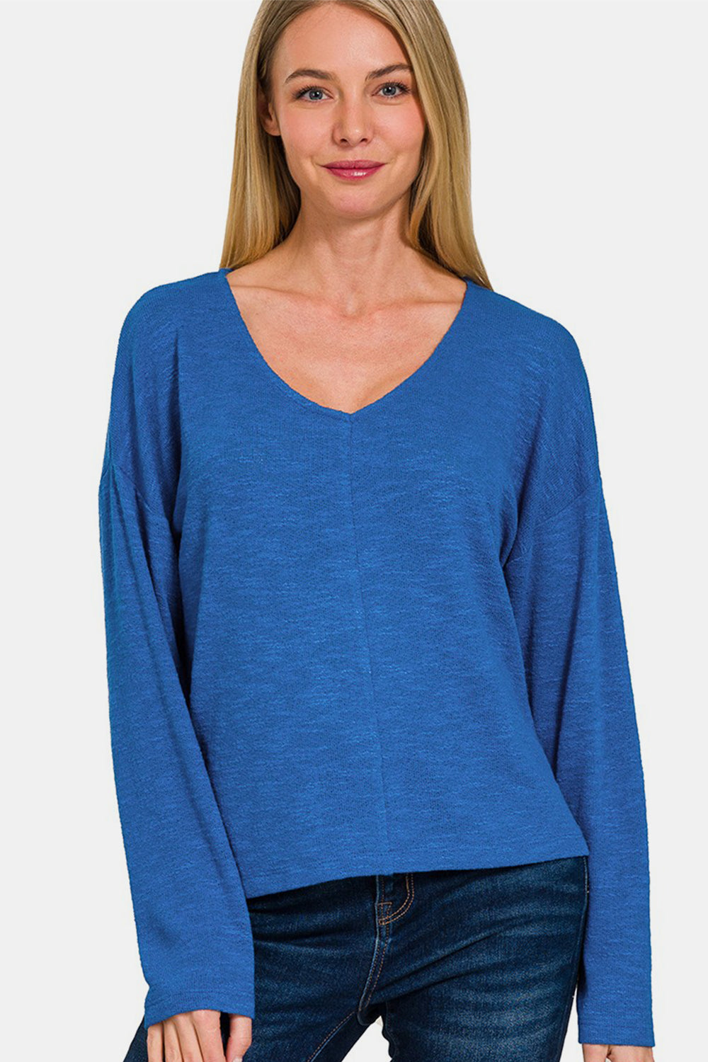 A person wearing a Zenana Dropped Shoulder Long Sleeve T-Shirt in blue and jeans stands against a plain background.