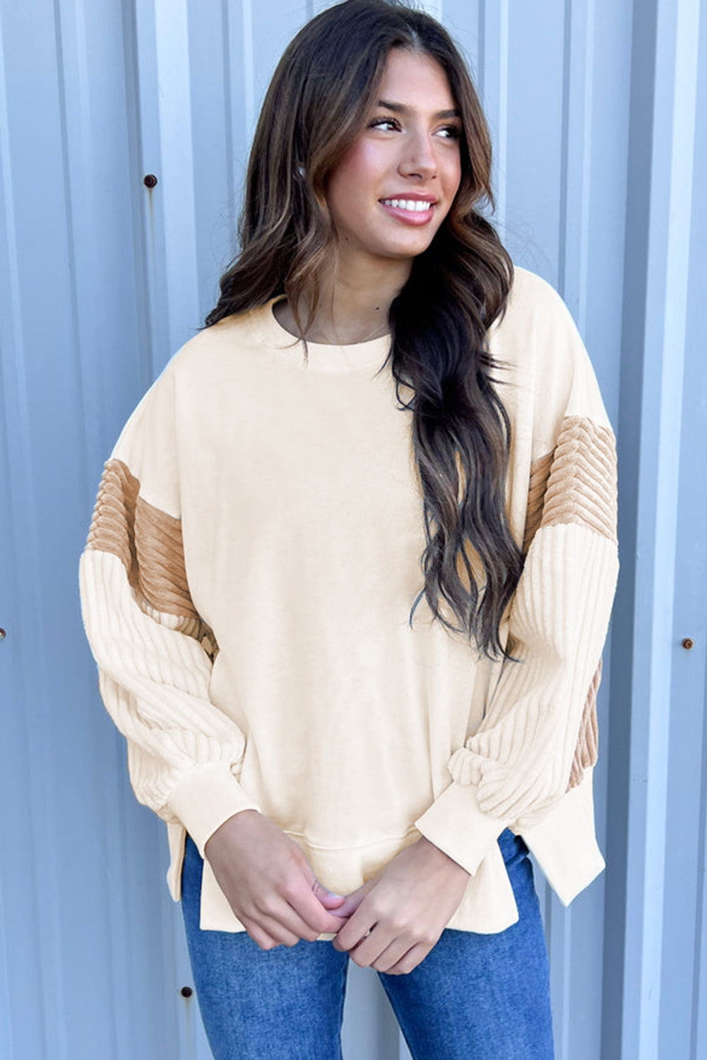 A person with long hair is wearing an Apricot Corduroy Patchwork Drop Shoulder Long Sleeve Sweatshirt, standing with their back to the camera against a light blue corrugated metal wall.