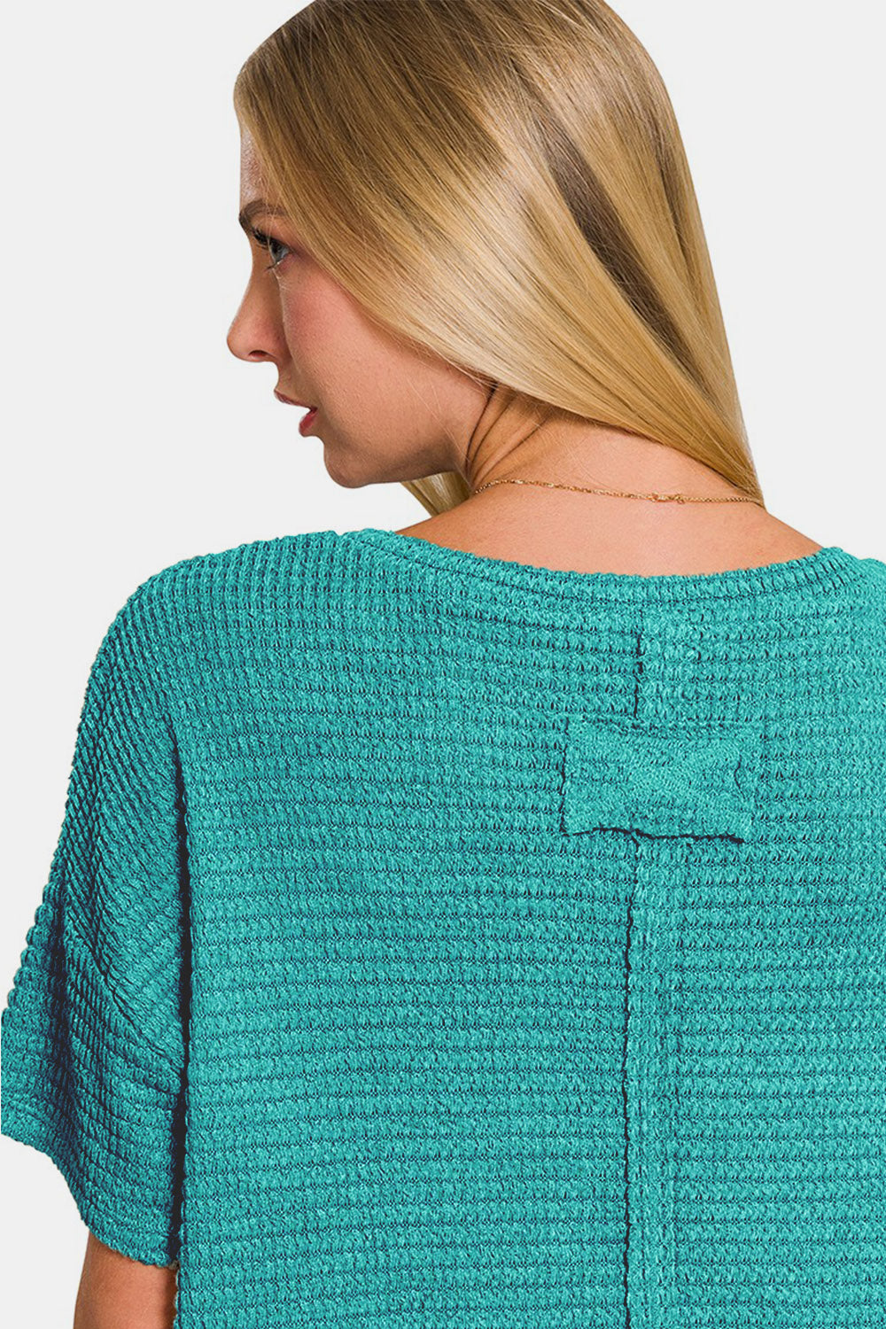 A person wearing a Zenana Drop Shoulder Short Sleeve Jacquard Knit Top in teal, paired with blue jeans, smiling against a plain white background.