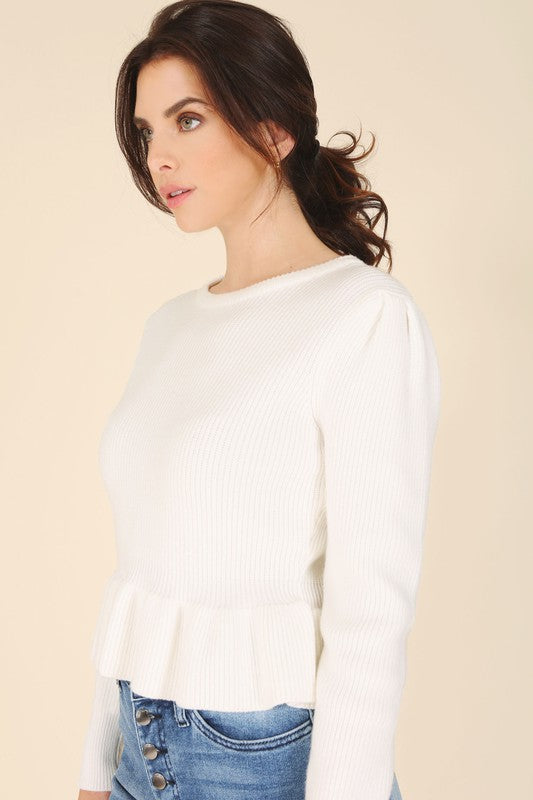 A woman stands elegantly in front of a white panel background, wearing the Peplum sweater top in red, featuring a round neck and puff sleeves, paired with a black skirt that has a side slit.