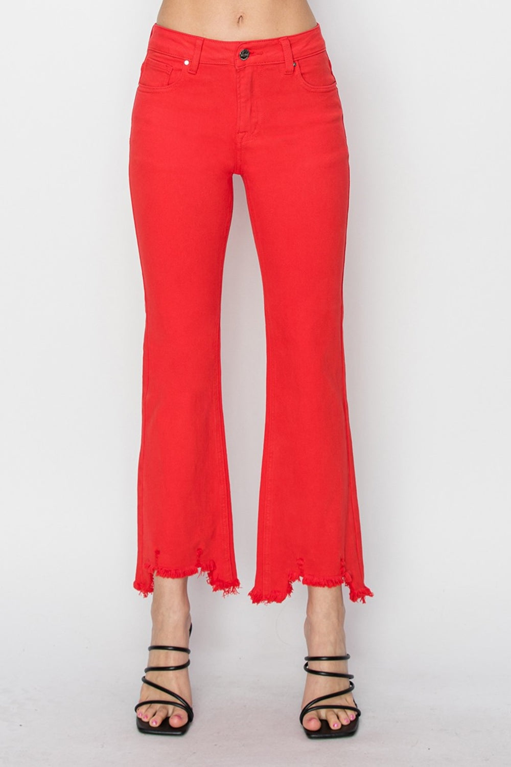 A person is wearing the RISEN Raw Hem Bootcut Jeans with Pockets in bright red, paired with a white top and black strappy high-heeled sandals. The image focuses on the stylish and functional lower half of the body.