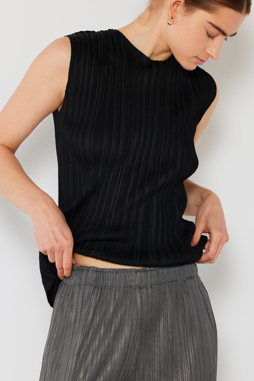 Person wearing a Marina West Swim Pleated Sleeveless Crewneck Tank and a gray pleated skirt, standing against a white background.