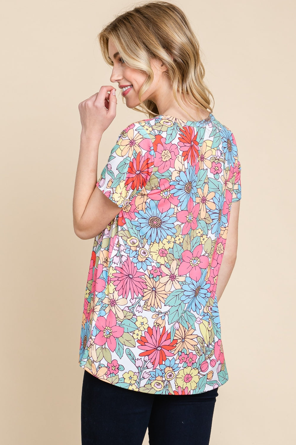 A woman wearing a vibrant BOMBOM Floral Short Sleeve T-Shirt and dark pants, posing against a beige background.