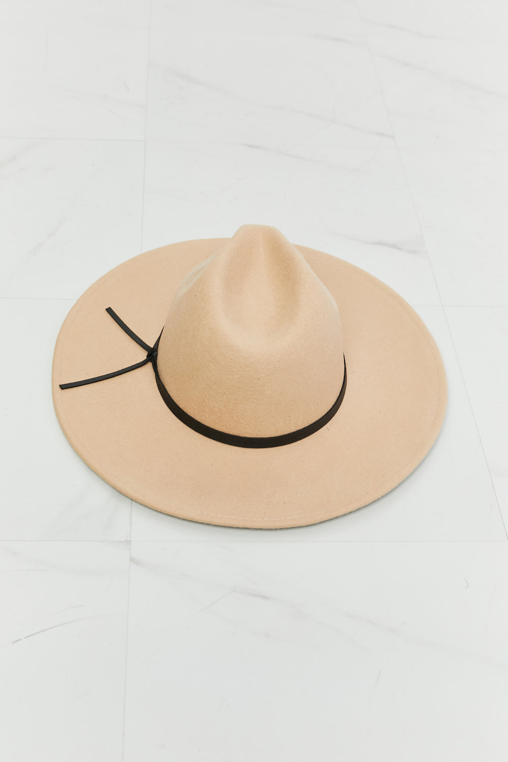 Wearing the Fame Make It Work Fedora Hat in light beige with faux leather detailing and a white tank top, a person smiles slightly while tilting their hat with one hand.