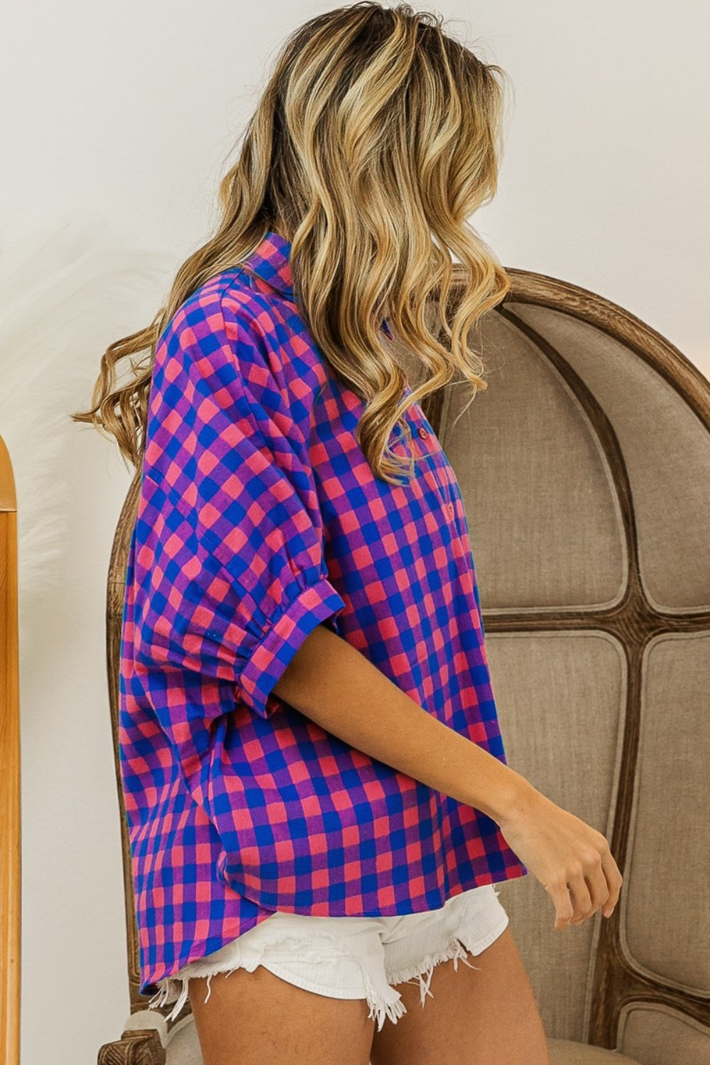 Person wearing a BiBi Plaid Button Up Dolman Sleeve Shirt in blue and pink with white shorts, standing in front of a wooden chair.