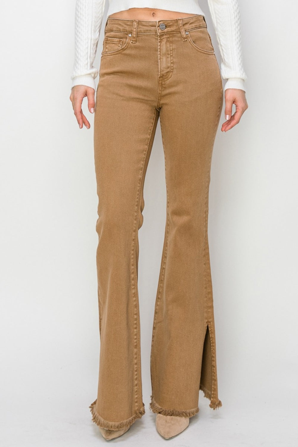 Wearing the RISEN Bailey Full Size High Waist Side Slit Flare Jeans with frayed hems, a person pairs them with beige boots against a white background.