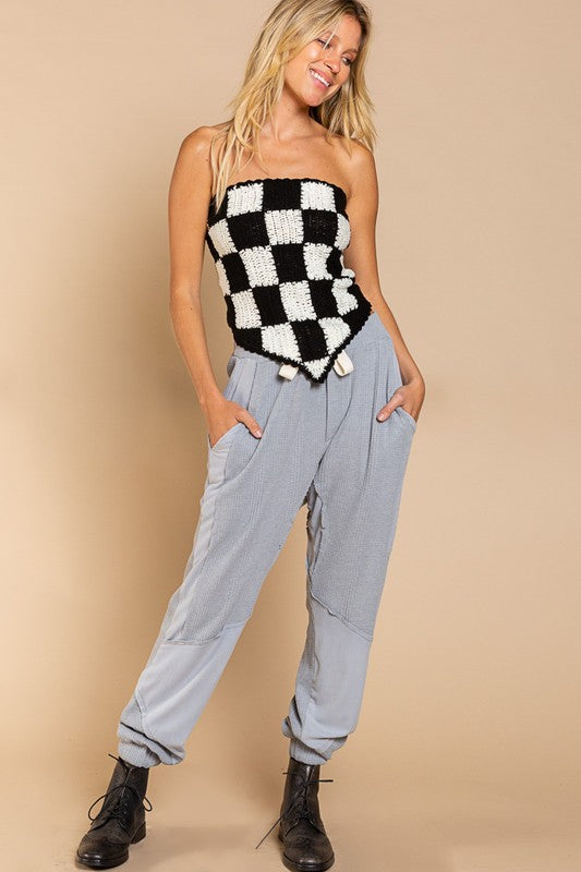 A woman stands against a beige background, wearing the playful Checkerboard Pattern Tube Top Sweater in pink and white, which beautifully contrasts with her blue jeans.