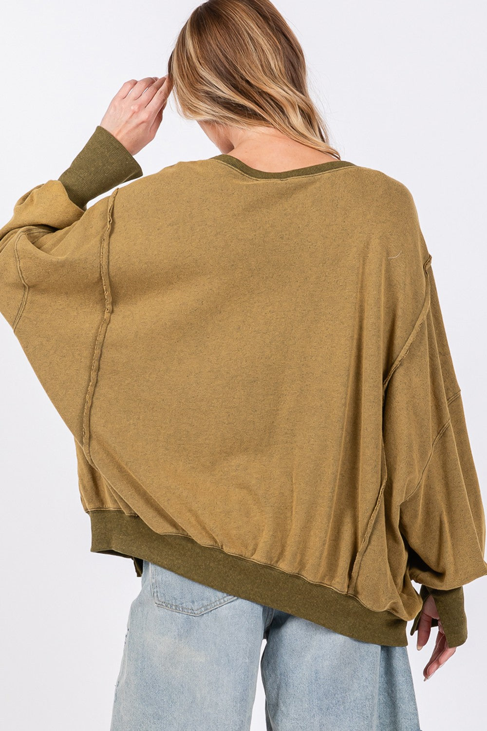 A person wearing a loose, oversized mineral wash SAGE + FIG Side Slit Sweatshirt in olive green, light blue jeans, and a black cap poses against a plain background.