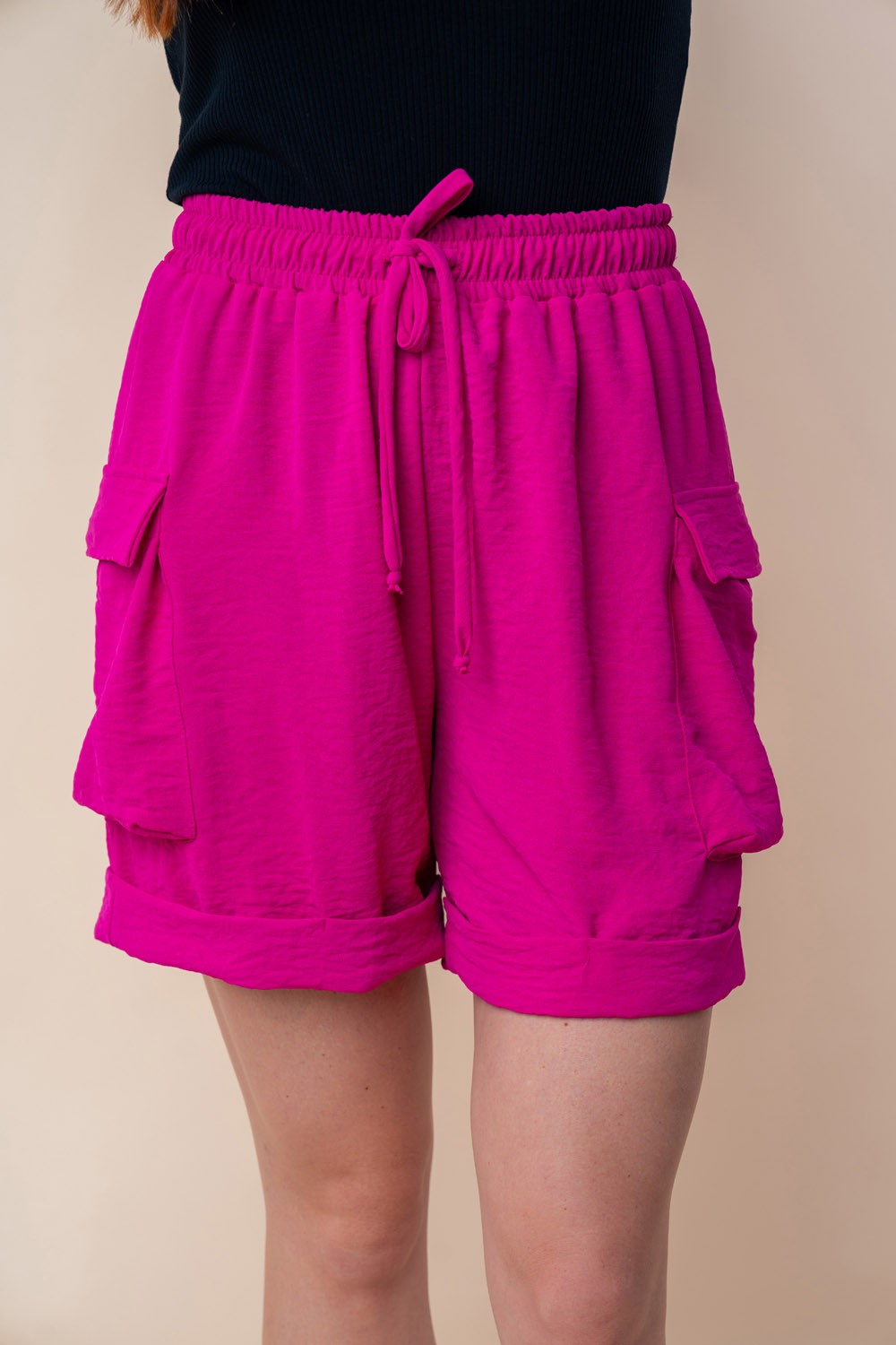 A person is wearing the White Birch High Waisted Drawstring Knit Cargo Shorts in bright pink, featuring side pockets and a drawstring waistband.