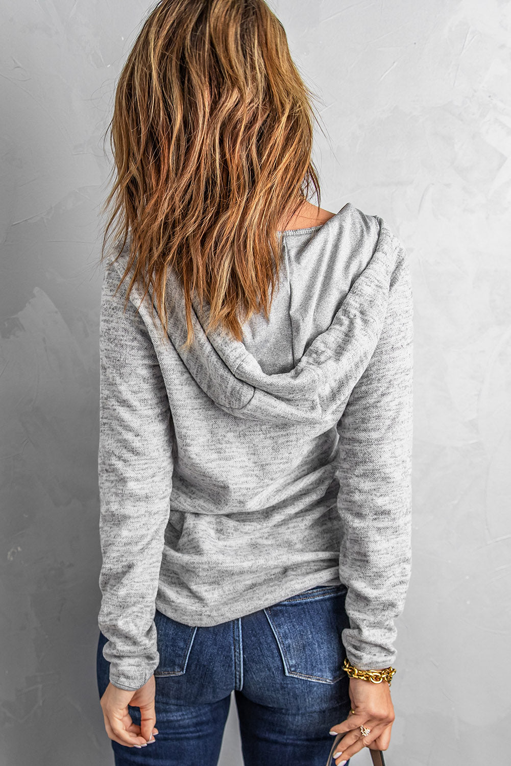 A person with wavy hair, wearing a Pocket Design Buttoned Casual Hoodie in gray and blue jeans, is standing with their back to the camera, showcasing an athletic style.