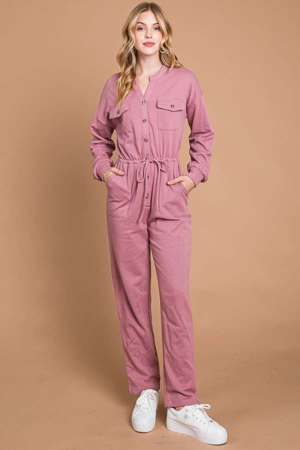 Against a beige background, an individual models the Culture Code Full Size Button Up Drawstring Waist Straight Jumpsuit, which features a stylish pink design with pockets and a chic drawstring waist.