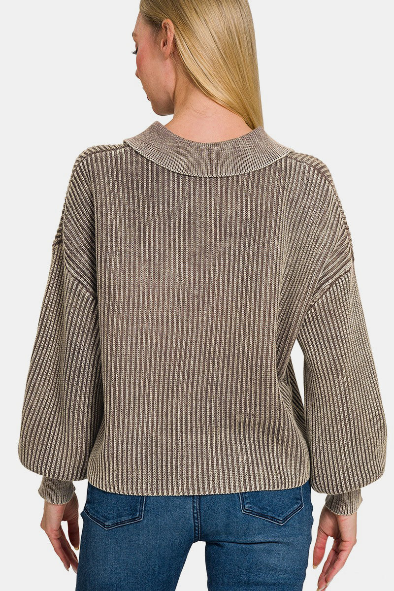 A woman with long blonde hair wearing the Zenana Washed Half Button Long Sleeve Sweater, made of 100% cotton and featuring a striped oversized design, pairs it with jeans as she stands against a plain background, smiling with one hand touching the sweater's collar.